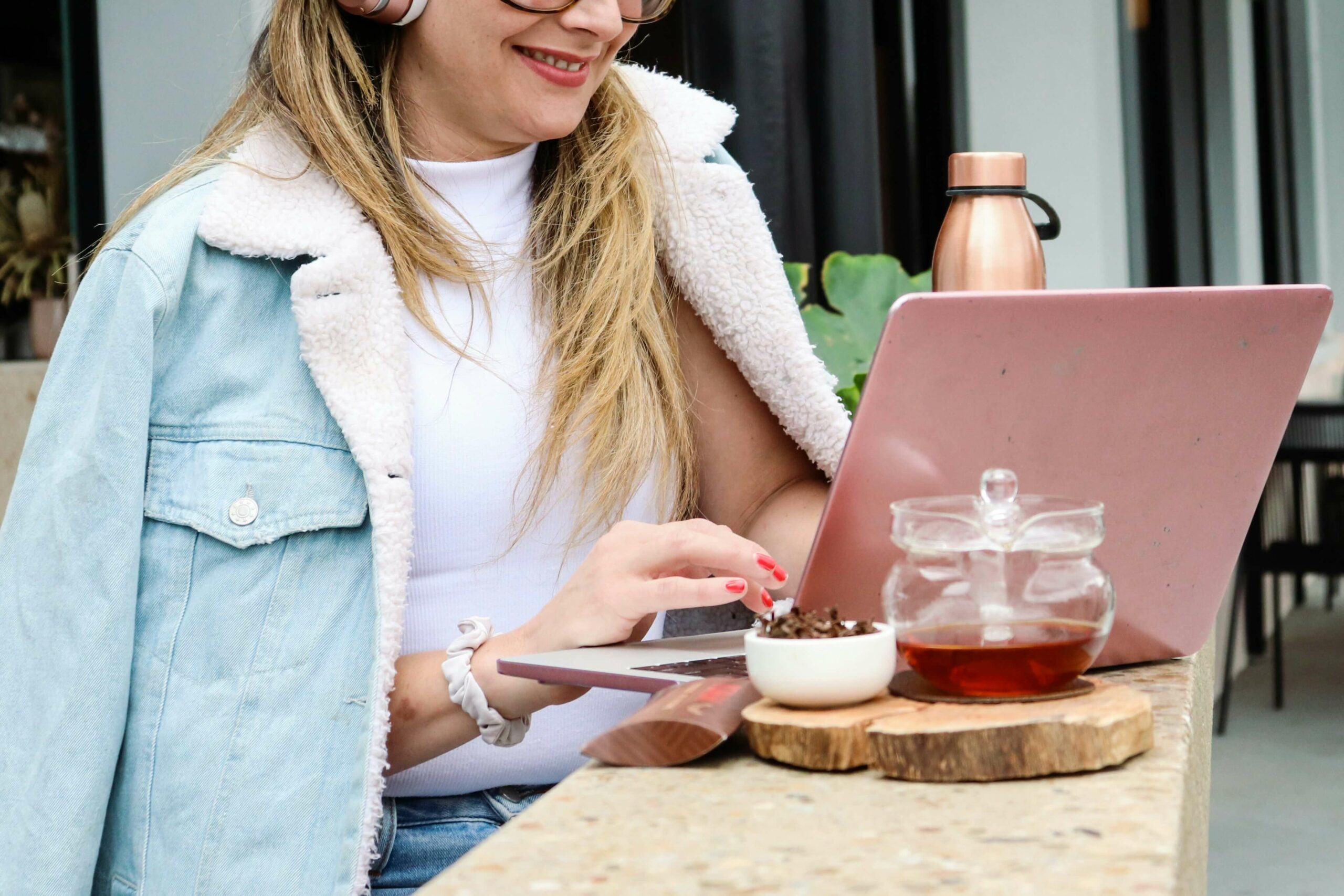 Woman sitting outside a cafe typing on an open laptop, with filtered tea on the side.